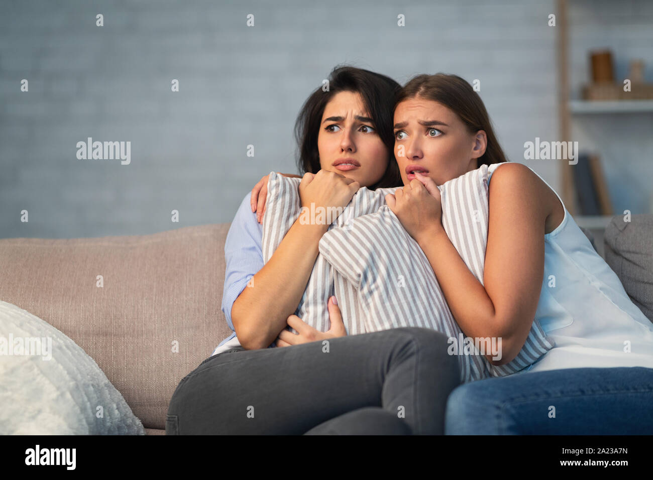Two Scared Girls Hugging Pillows Sitting On Couch Alone At Home While Somebody Trying Break Into House. Free Space Stock Photo