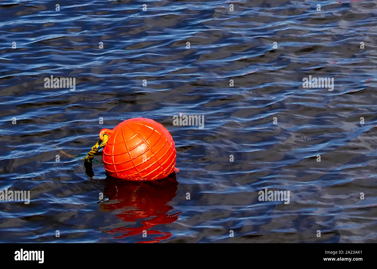 One bright orange buoy floating on lake water surface. Close up of range safety buoys in a lake with small waves on water surface. Stock Photo