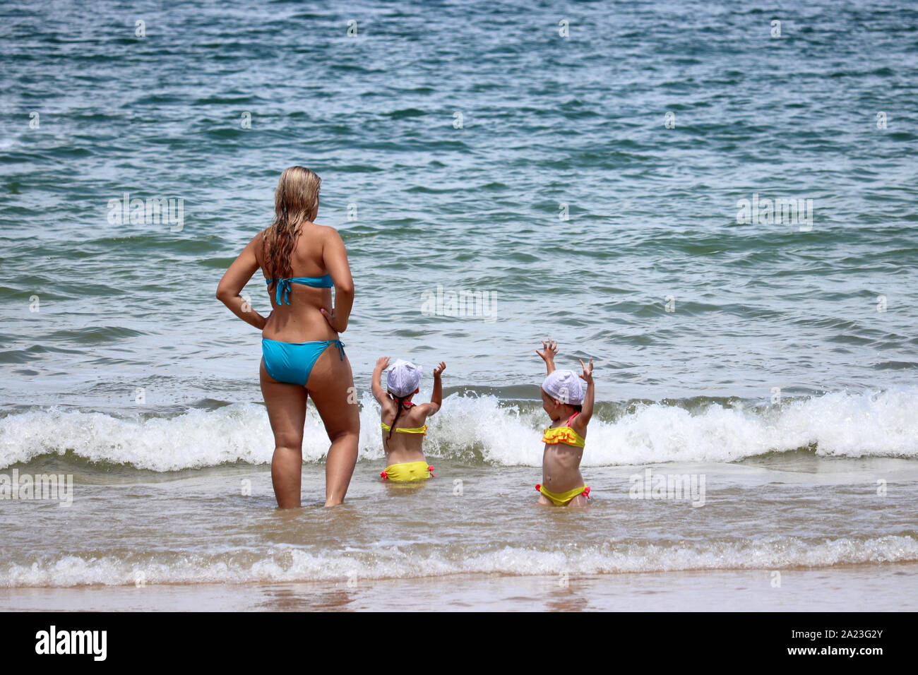 Mother and joyful children go swimming in the blue sea. Woman with two little daughters on the beach, concept of family leisure, holidays, single mom Stock Photo