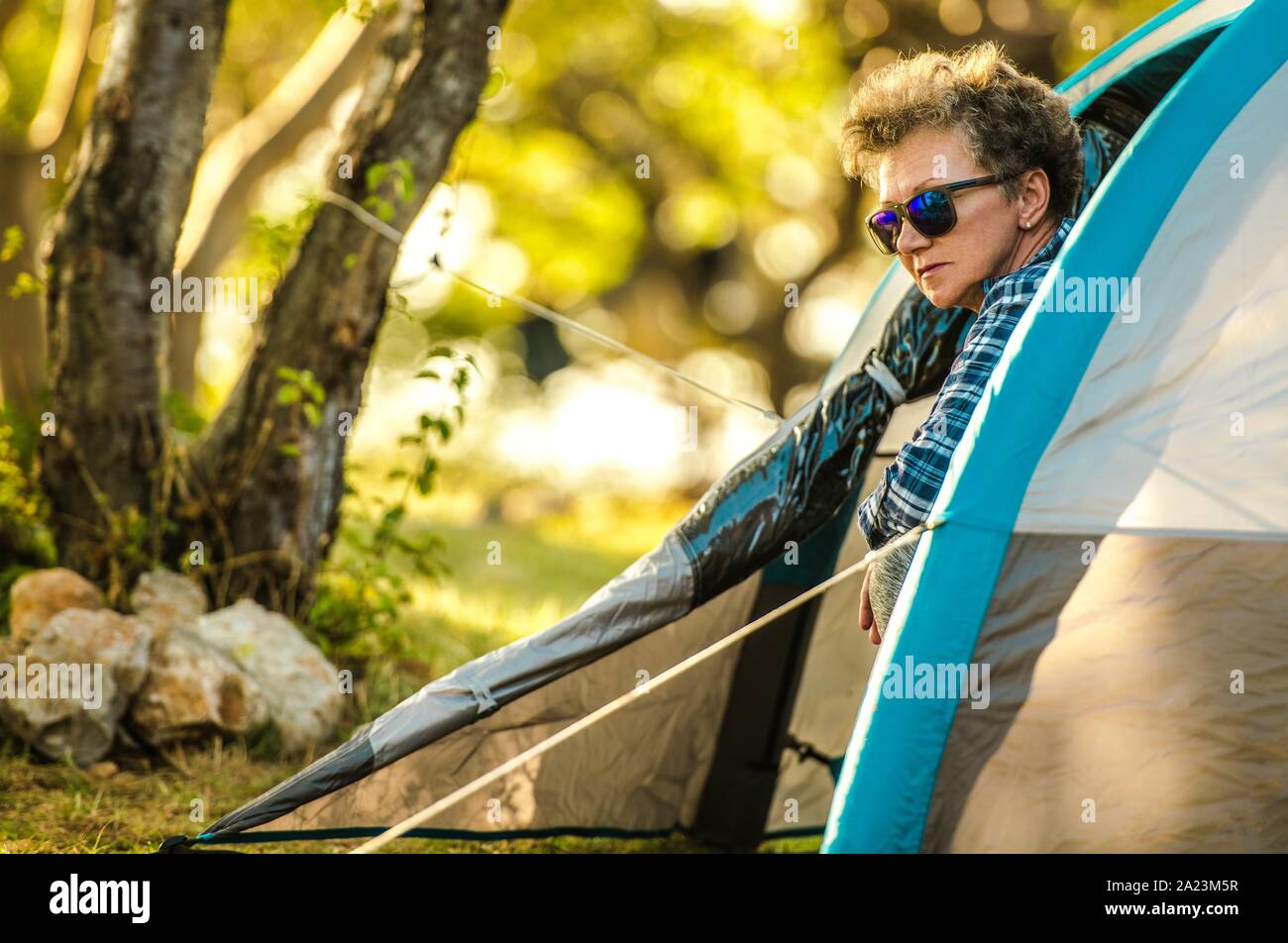 Senior Woman Tent Camping. Caucasian Retired Woman in Her 60s Looking Outside From Her Tent. Campground Pitch. Summer Vacation. Stock Photo