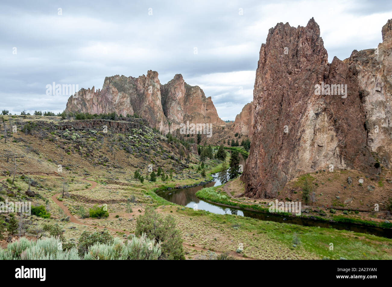 Crooked River winds through Smith Rock State Park in early summer, grass still green beside it and moody clouds above. Stock Photo