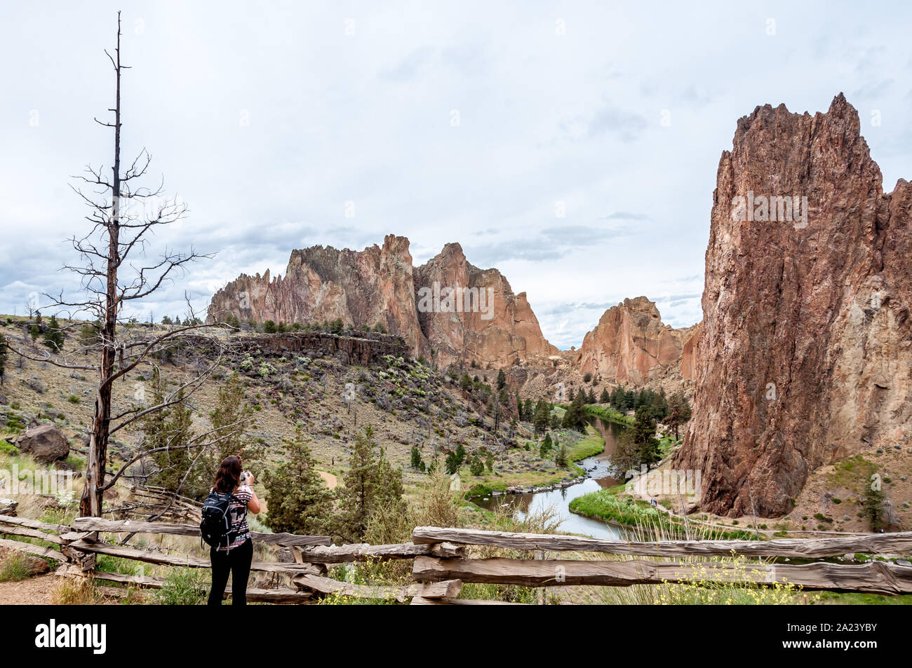 At Smith Rock State Park in Central Oregon, a woman hiker stops to take a photo of the steep rock faces towering above the river. Stock Photo