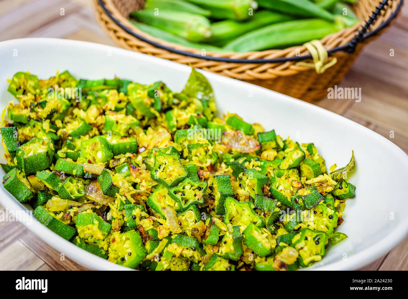 Closeup of Okra Stir Fry with grated coconut in an oval bowl with fresh Lady's fingers in a basket in the background Stock Photo