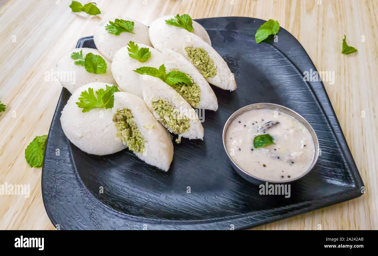 Steamed Idlis stuffed with chicken minced with mint leaves along with white coconut chutney in a black plate Stock Photo