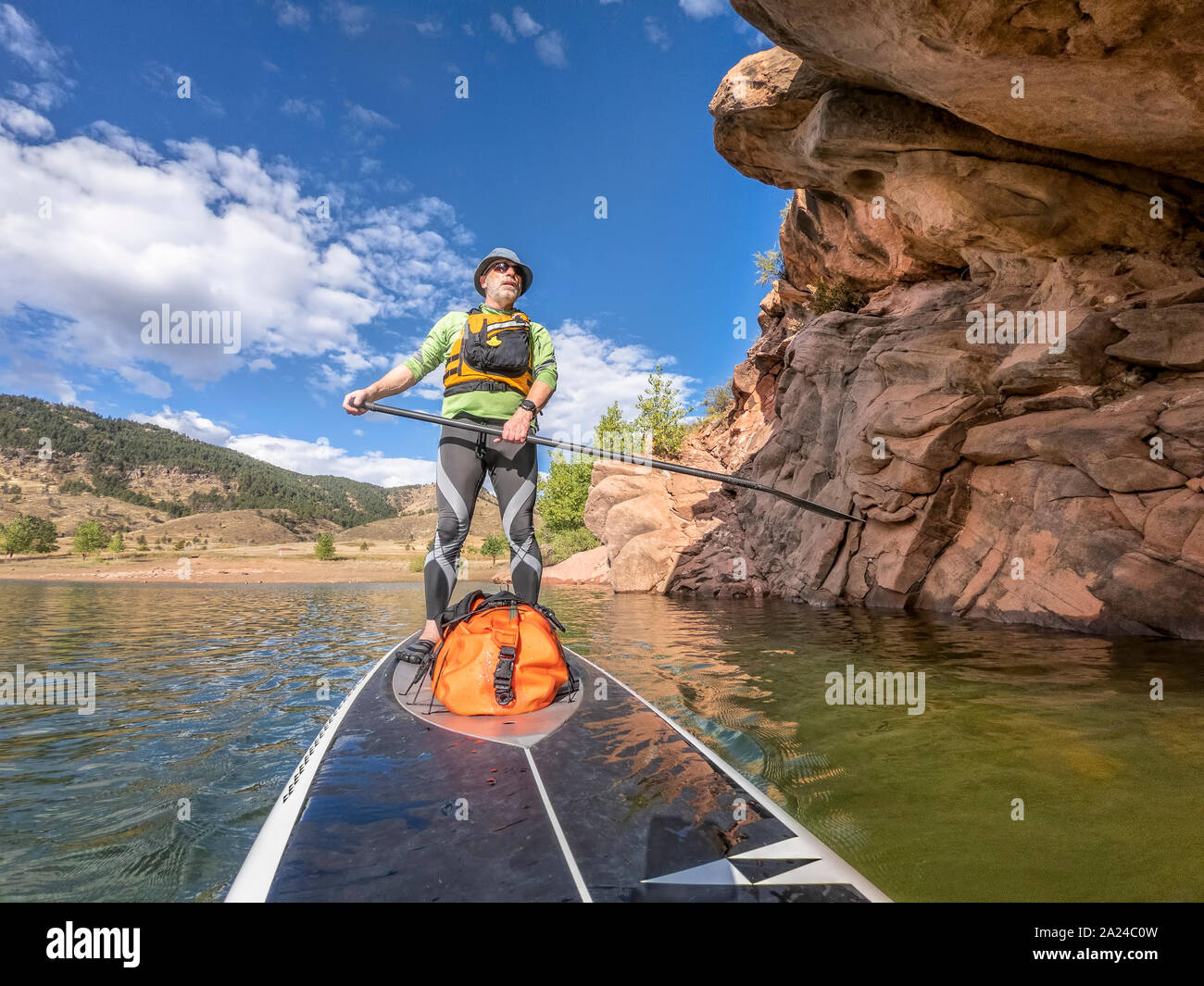 senior man paddling a stand up paddleboard  a mountain lake with sandstone cliffs - Horsetooth Reservoir , Colorado, in early fall scenery, POV with a Stock Photo