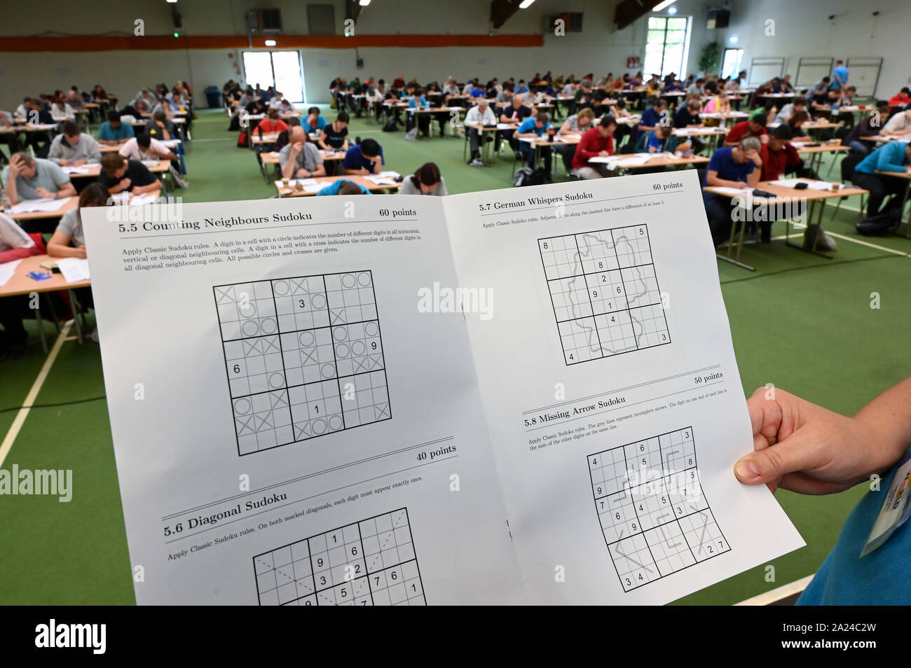 Kirchheim, Germany. 30th Sep, 2019. An organizer holds up a bow with Sudoku  puzzles, while in the background participants of the Sudoku World  Championship brood over their puzzles. Until Saturday, around 230
