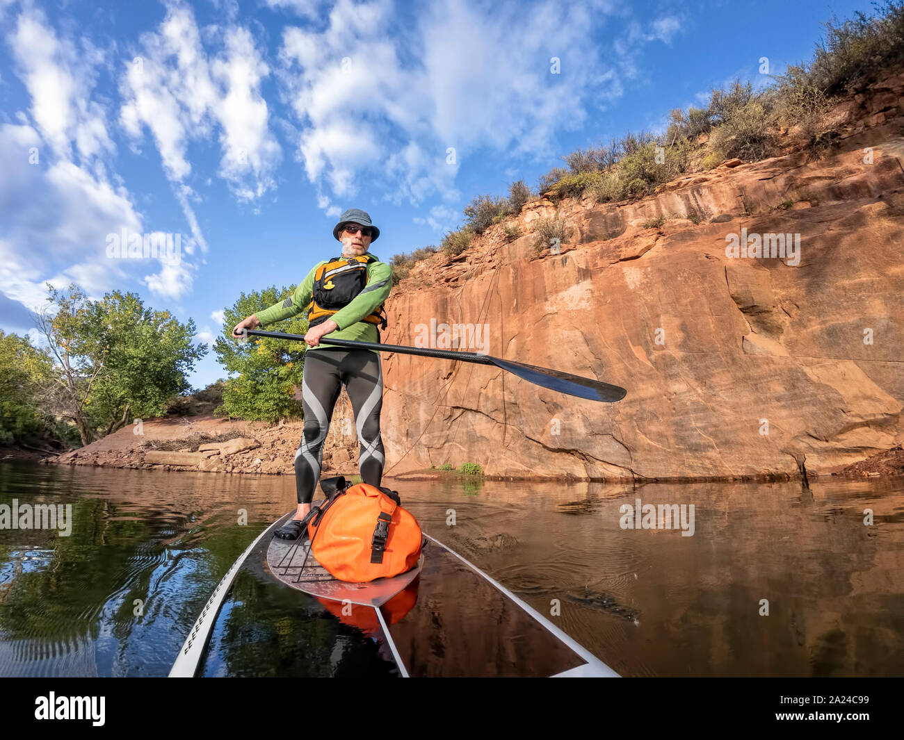 senior man paddling a stand up paddleboard  a mountain lake with sandstone cliffs - Horsetooth Reservoir , COlorado, in early fall scenery Stock Photo
