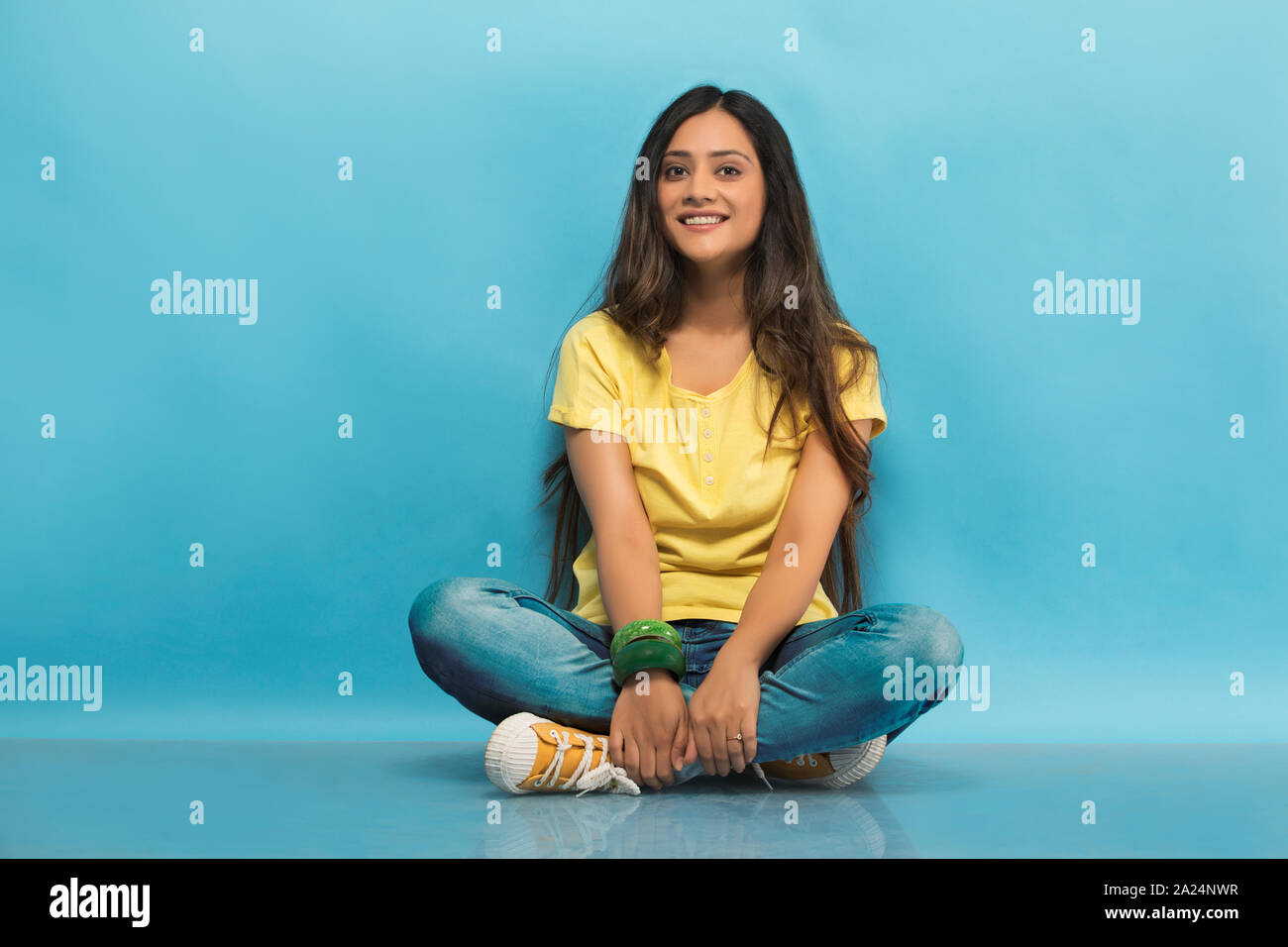 Smiling teenage girl in jeans and t-shirt sitting cross legged on the ...