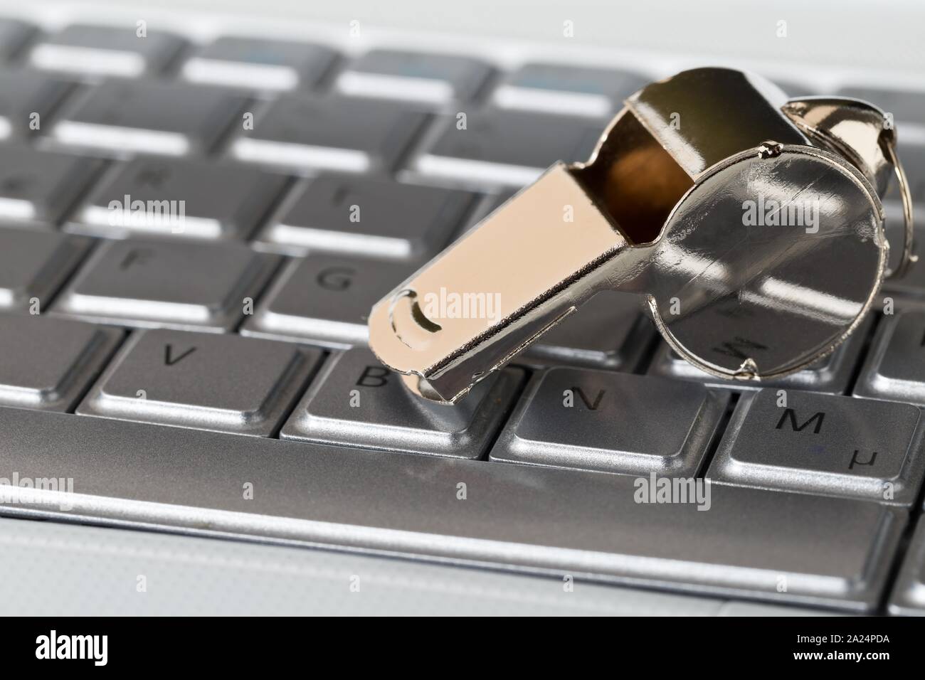 Chrome whistle on top of laptop computer keyboard - whistleblower concept, selective focus Stock Photo