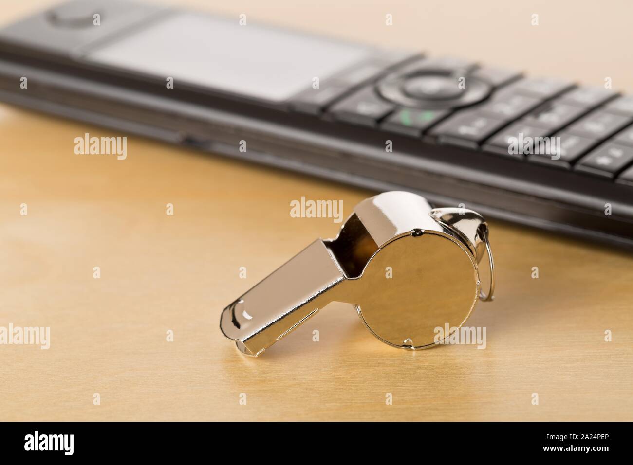 Chrome whistle with telephone on wooden office desk - whistleblower concept, selective focus Stock Photo