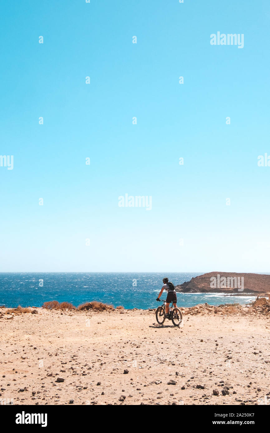 person on mountain bike bicycle in desert landscape near coast with ocean background Stock Photo
