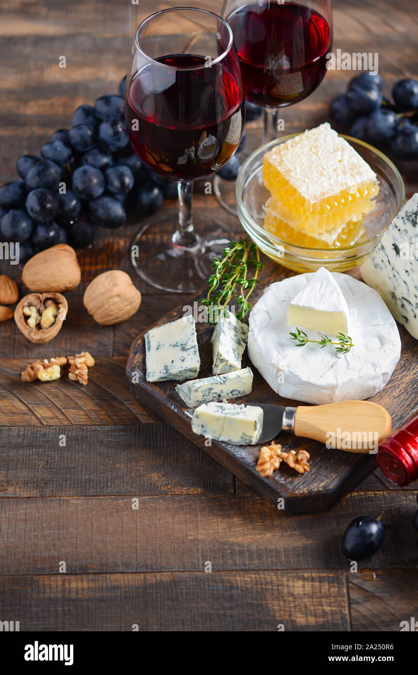 Cheese plate with grapes, honey, nuts and red wine on a wooden table. Stock Photo