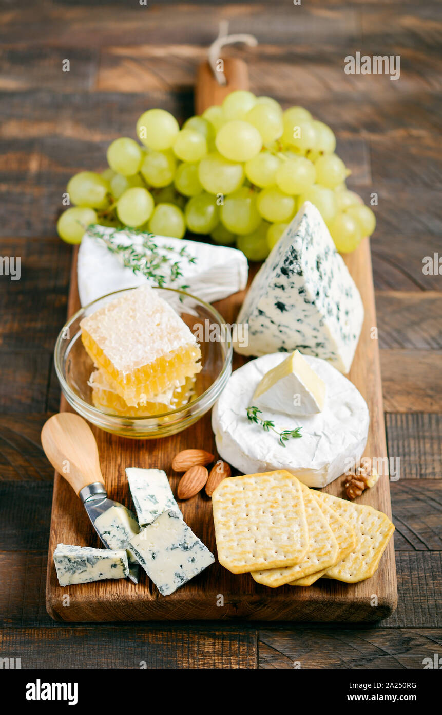 Cheese plate with grapes, crackers, honey and nuts on a wooden table. Stock Photo