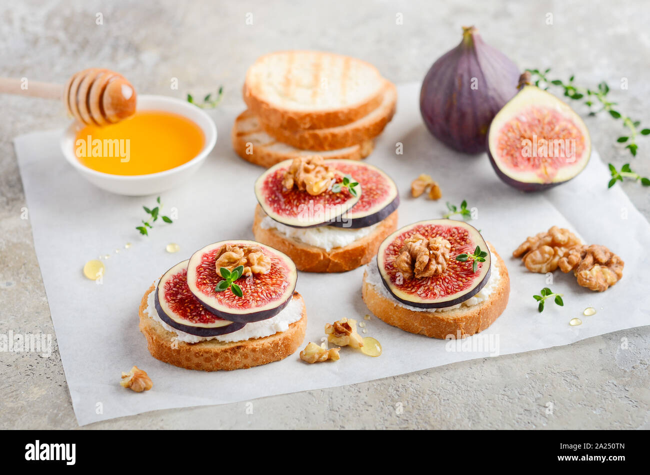 Bruschetta with fresh ricotta cheese, figs, nuts, thyme and honey on gray concrete background. Stock Photo