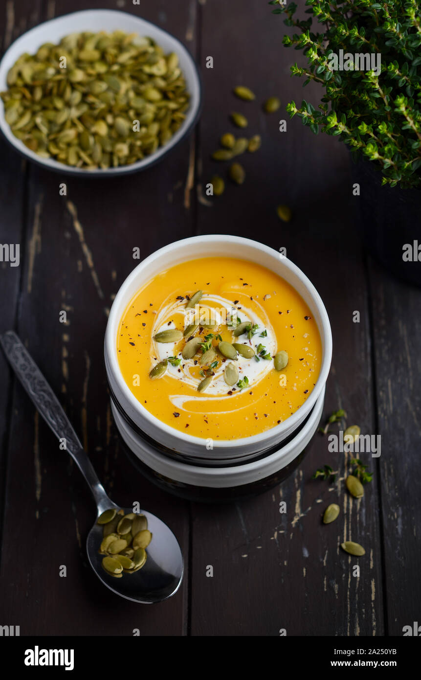 Pumpkin cream soup with cream and pumpkin seeds on old rustic table. Stock Photo