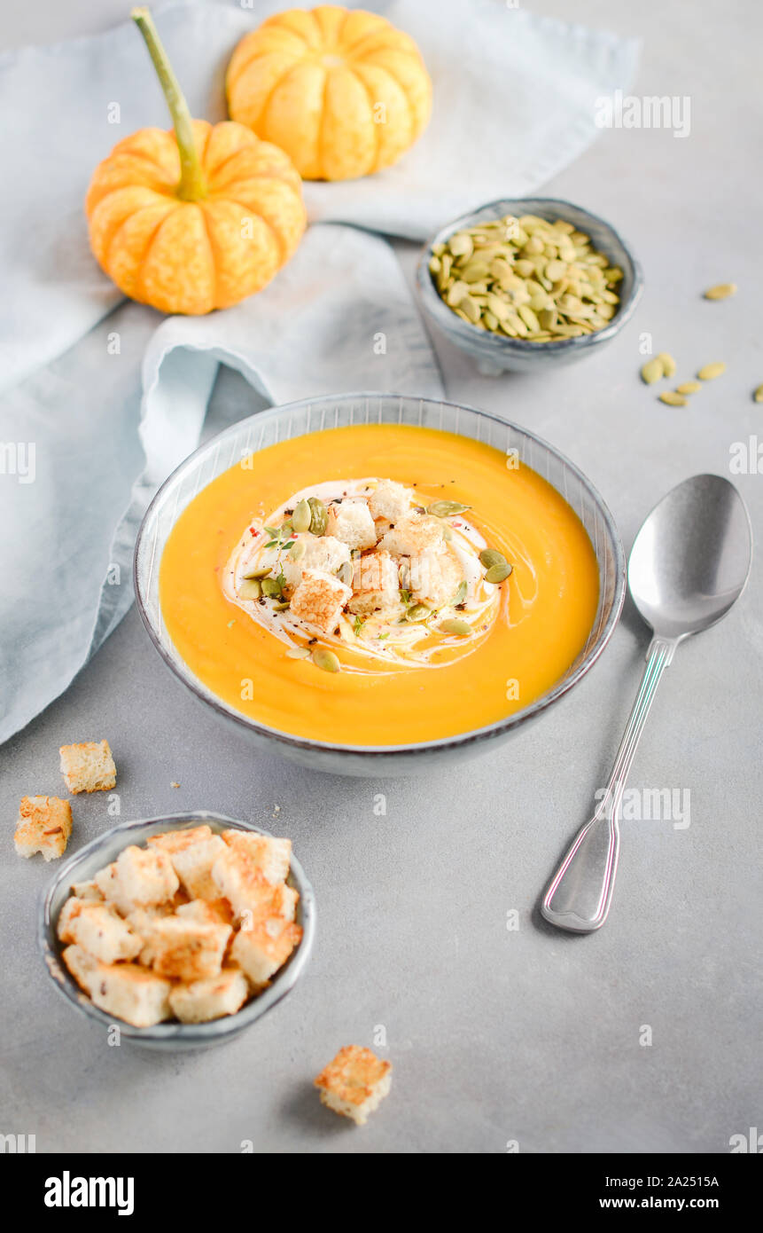 Pumpkin soup with cream, croutons, pumpkin seeds and thyme on a gray concrete or stone background. Stock Photo