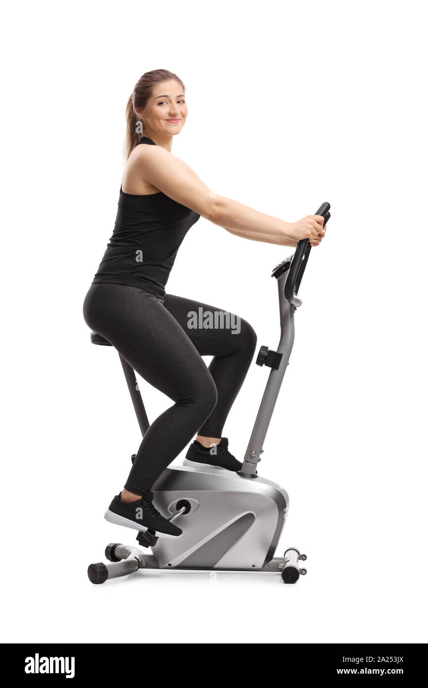 Full length shot of a young woman riding a stationary bike and smiling at the camera isolated on white background Stock Photo