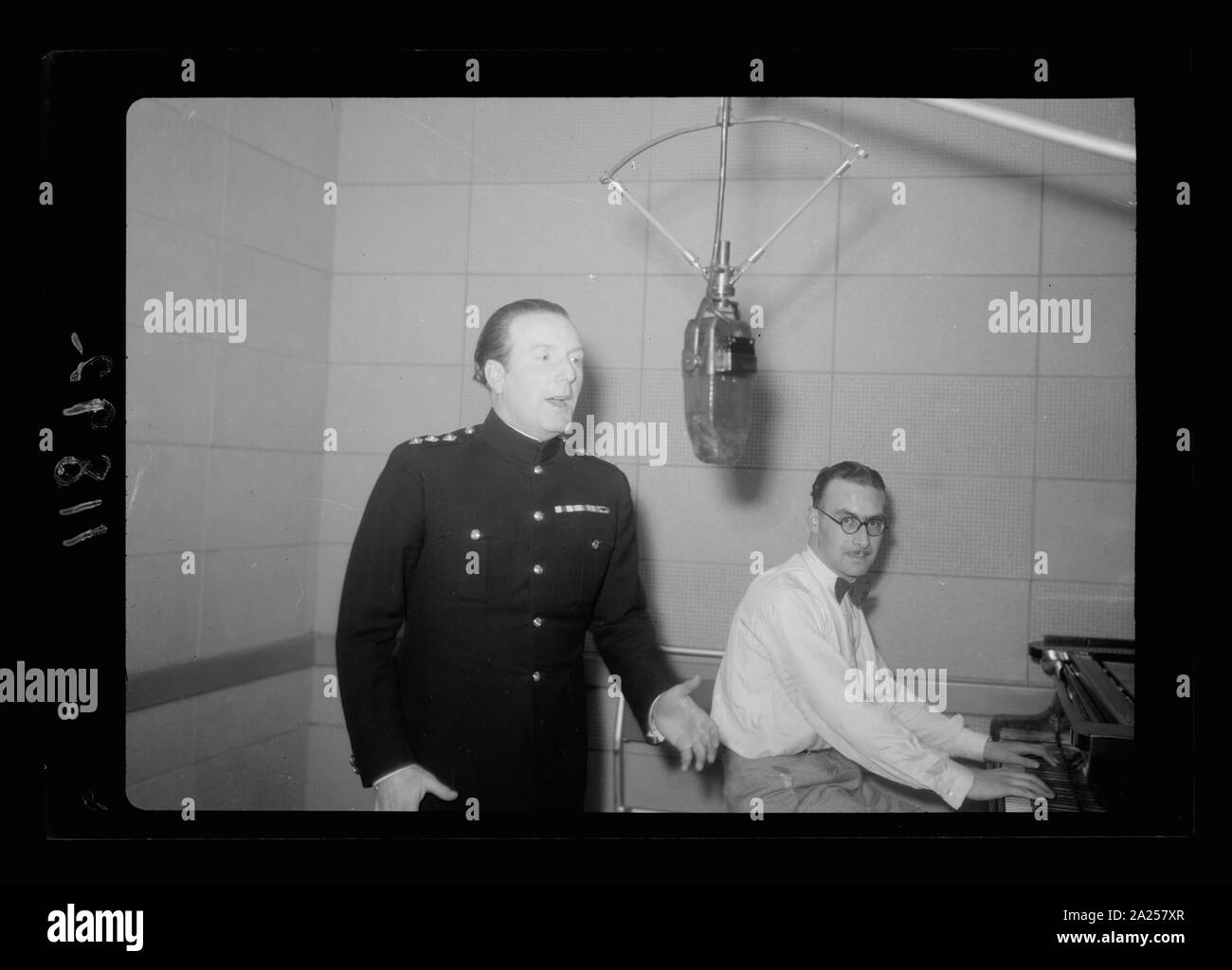 Photo taken in Palestine Broadcasting Service Studios, Jerusalem. Captain Lance Fairfax at mic. i.e., microphone, Lt. Watson at piano Stock Photo