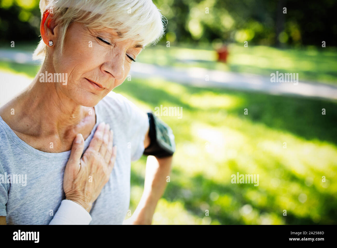 Senior woman with chest pain suffering from heart attack during jogging Stock Photo