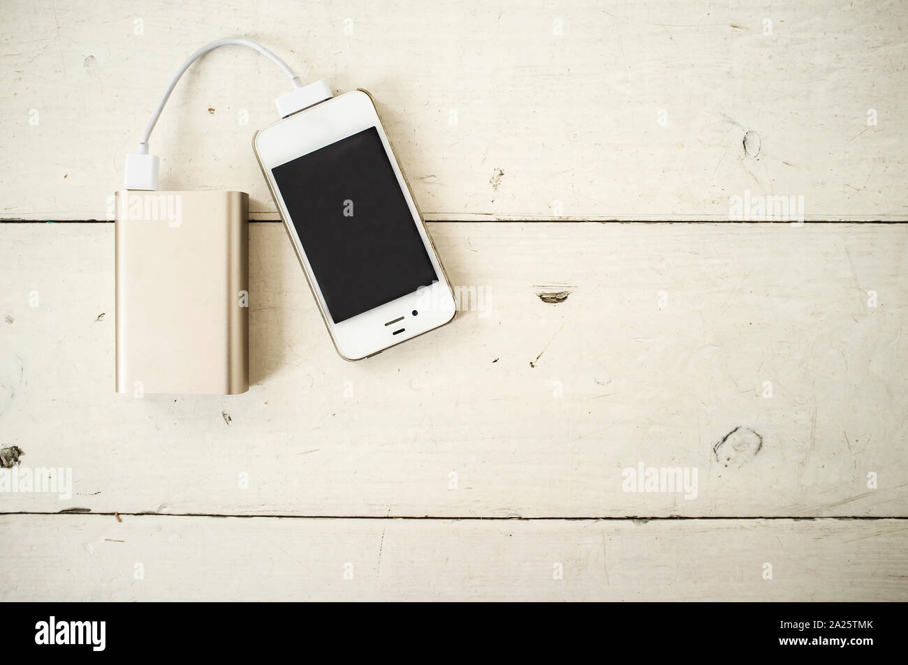 Smartphone is charged from the portable charging device for shabby the wooden table painted in white color Stock Photo