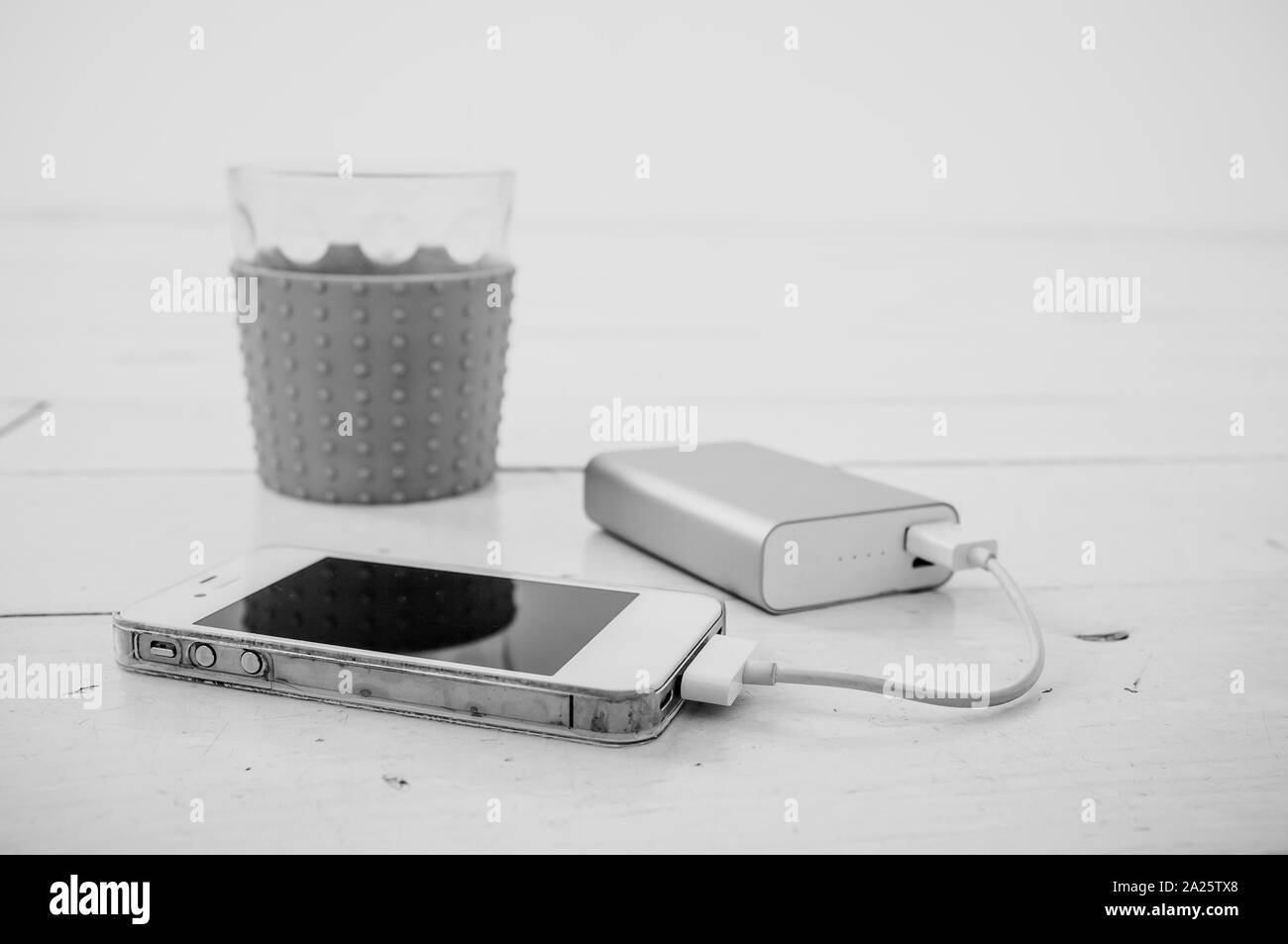 Smartphone being charged from a portable charging device, nearby there is a incomplete glass of tea with lemon Stock Photo