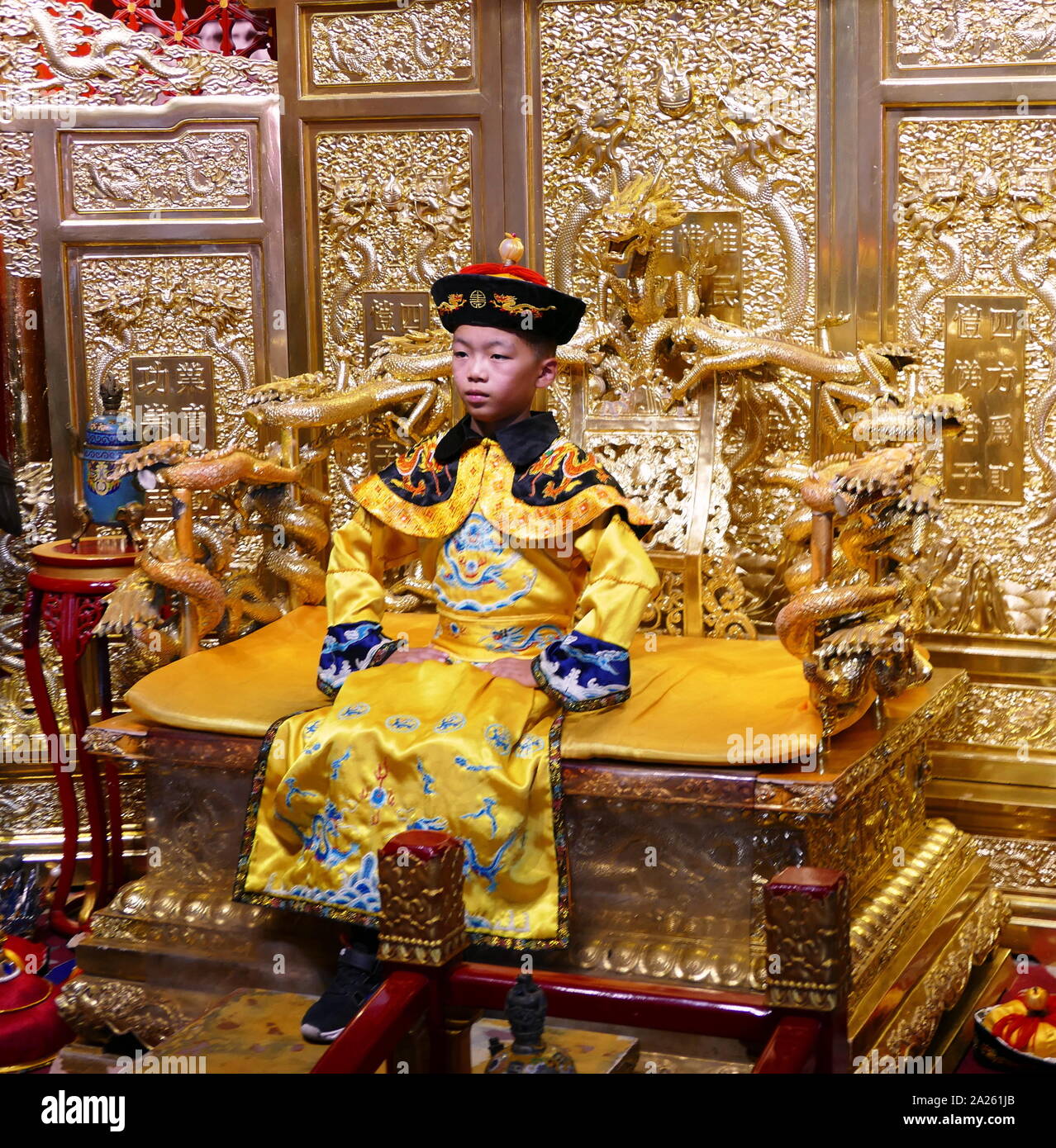 Child re-enacting the role of the last emperor of China Pu Yi seated on a replica of the Dragon Throne. As the dragon was the emblem of divine imperial power, the throne of the Emperor, who was considered a living god, was known as the Dragon Throne Stock Photo