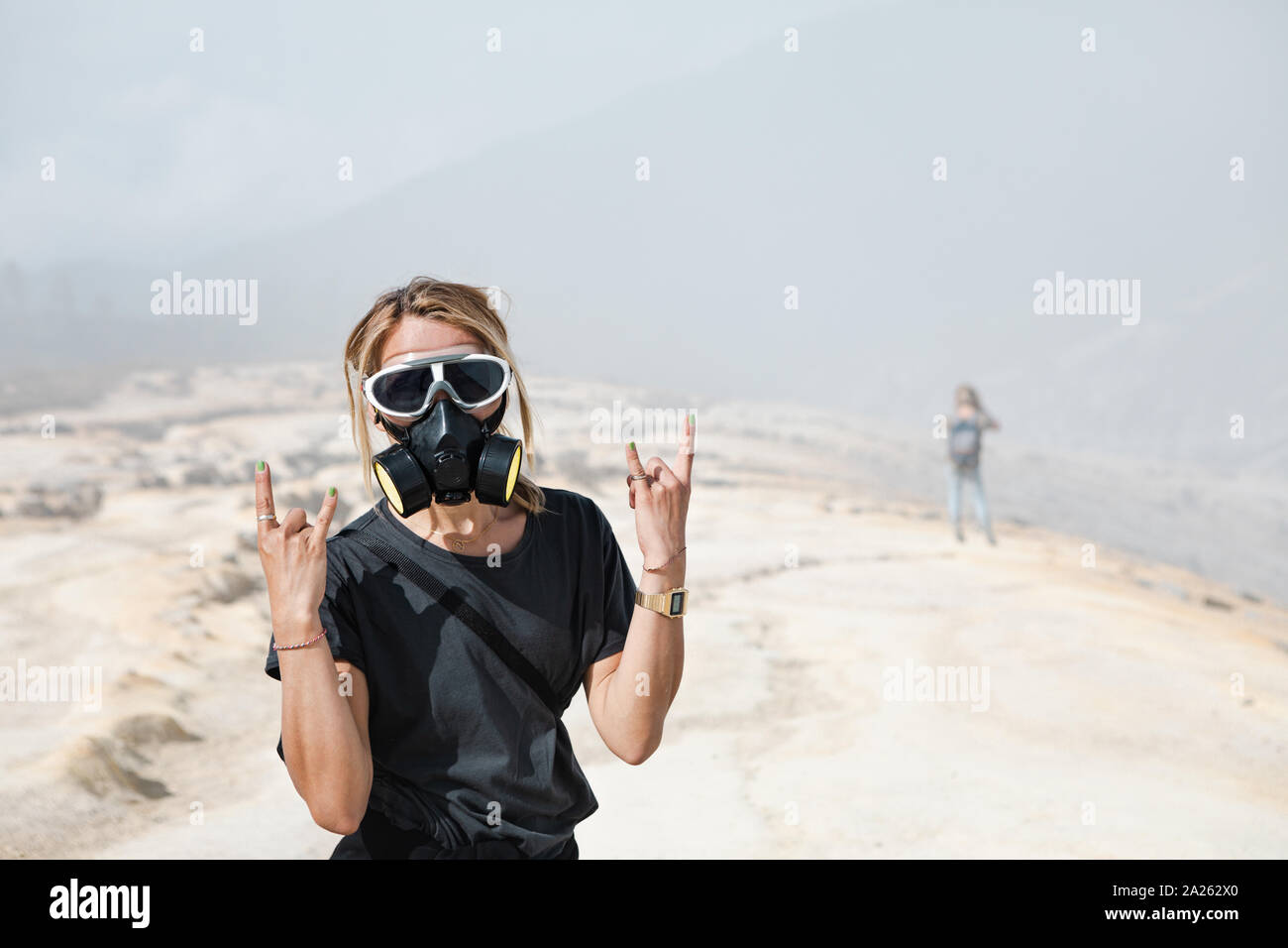 Young women in protective mask walking by wastelands around Kawah Ijen volcano crater. Post apocalypse landscape, clouds of toxic gases from volcano Stock Photo