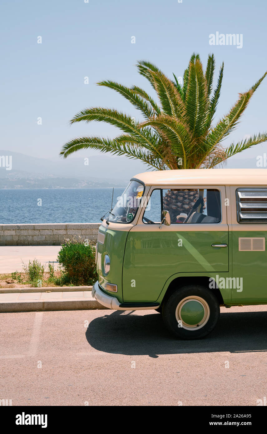 A retro vintage classic VW T2 Camper Van painted green and white on the coast next to a palm tree in the summer Stock Photo