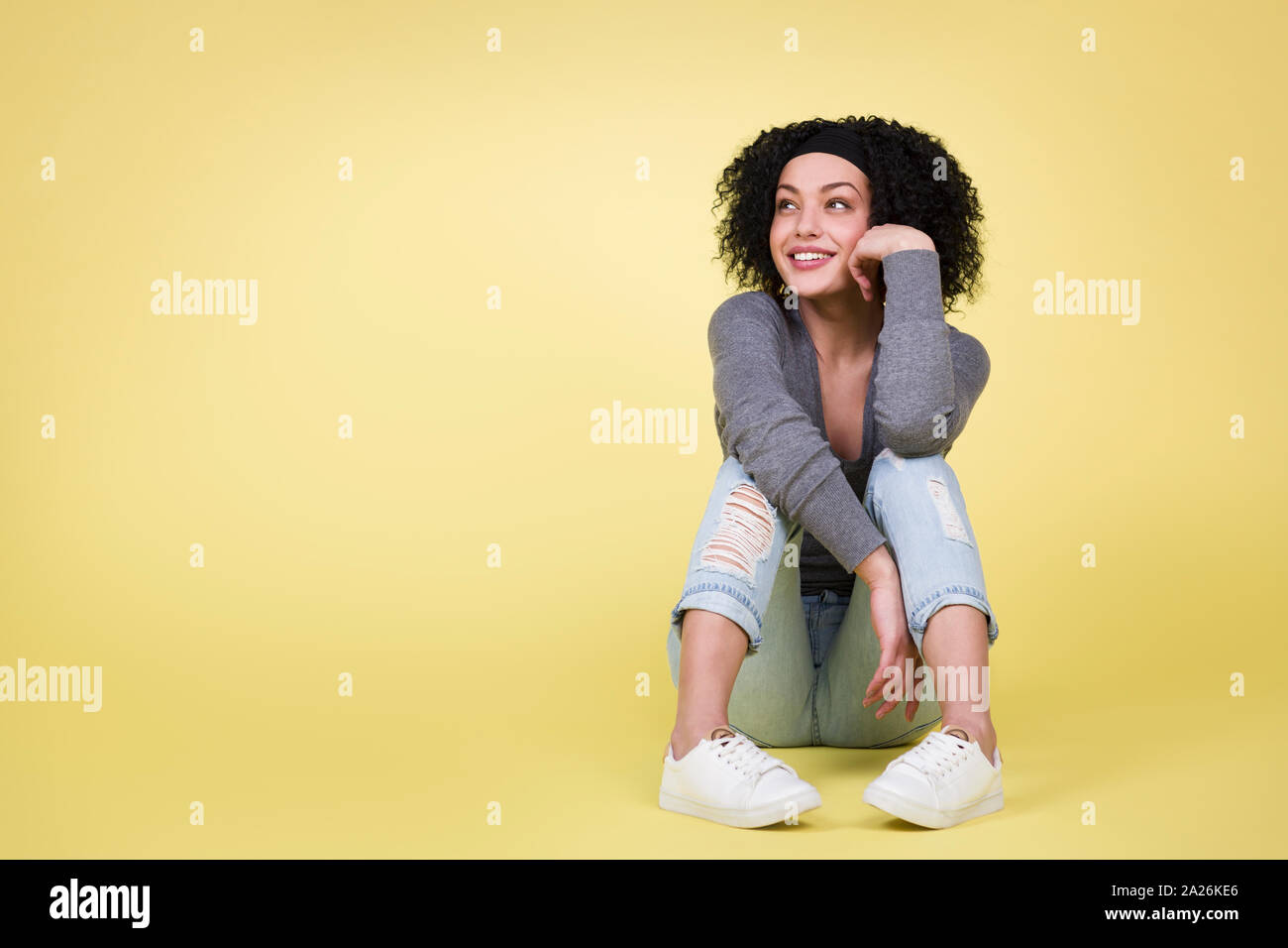 Joyful woman looking up sitting on isolated yellow background. Stock Photo