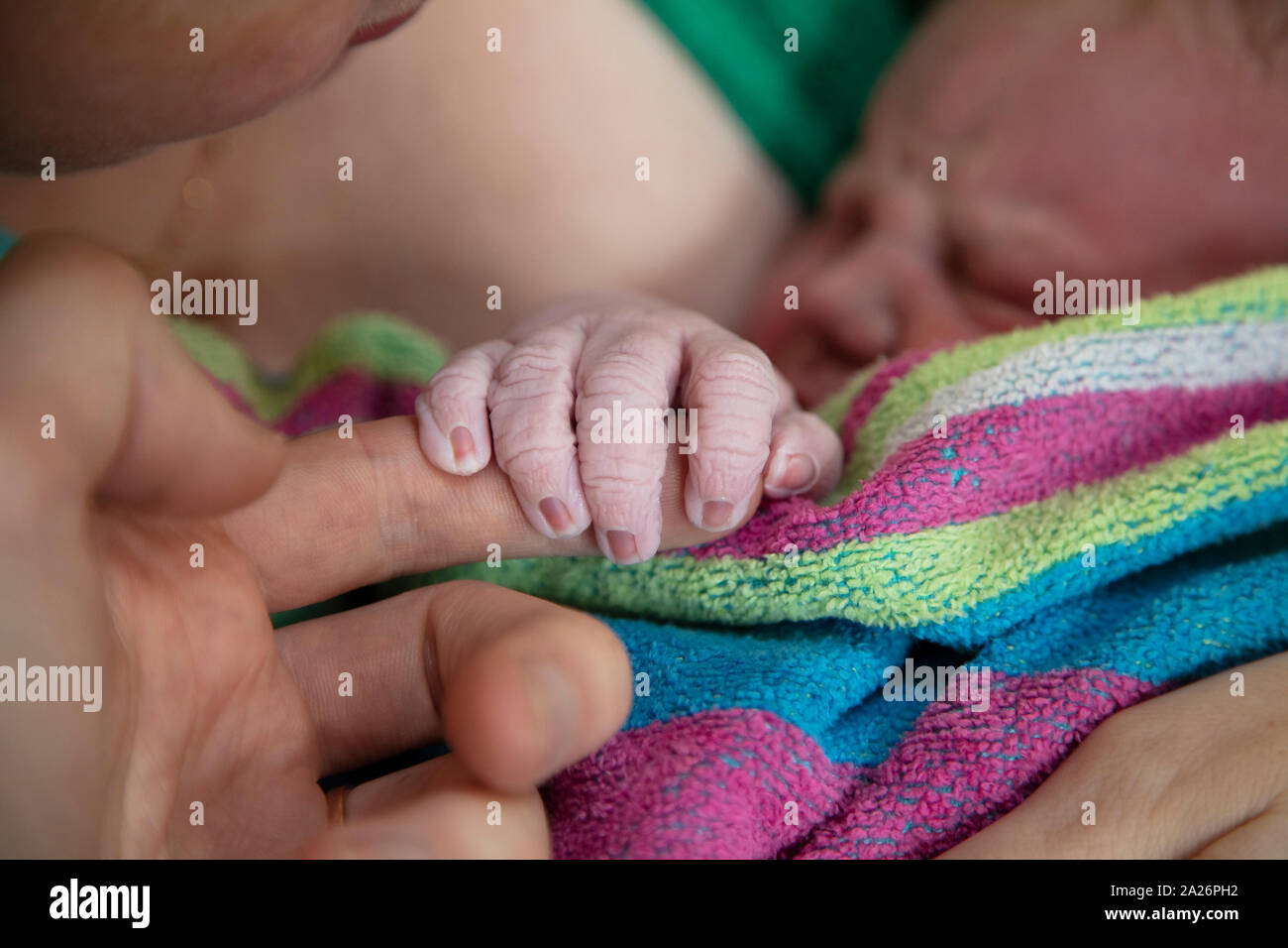A newborn baby holds onto their fathers finger after being born Stock Photo