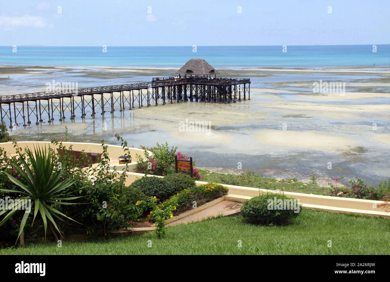 View of pier with a Lapa bar on beach and flowerbed with lawn, off the coast of Zanzibar, Unguja Island, Tanzania. Stock Photo