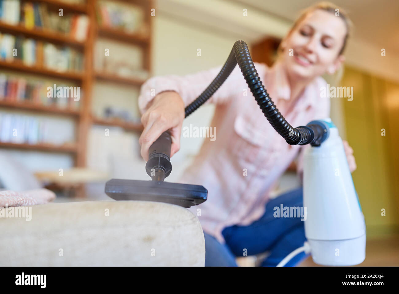 Cleaning lady with hand vacuum cleaner cleans upholstered furniture