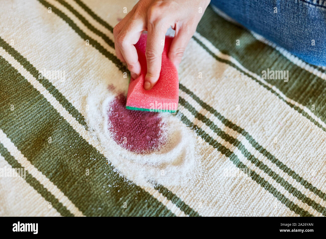 Hand with sponge while removing red wine stains with salt on carpet Stock Photo