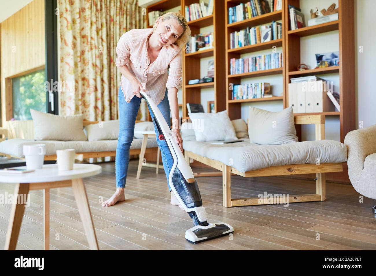 Young housewife or cleaning lady vacuuming parquet in the living room ...