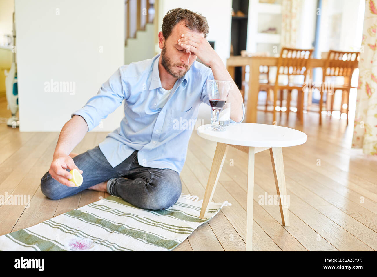 Hausmann sits frustrated in front of a carpet with red wine patches at home Stock Photo