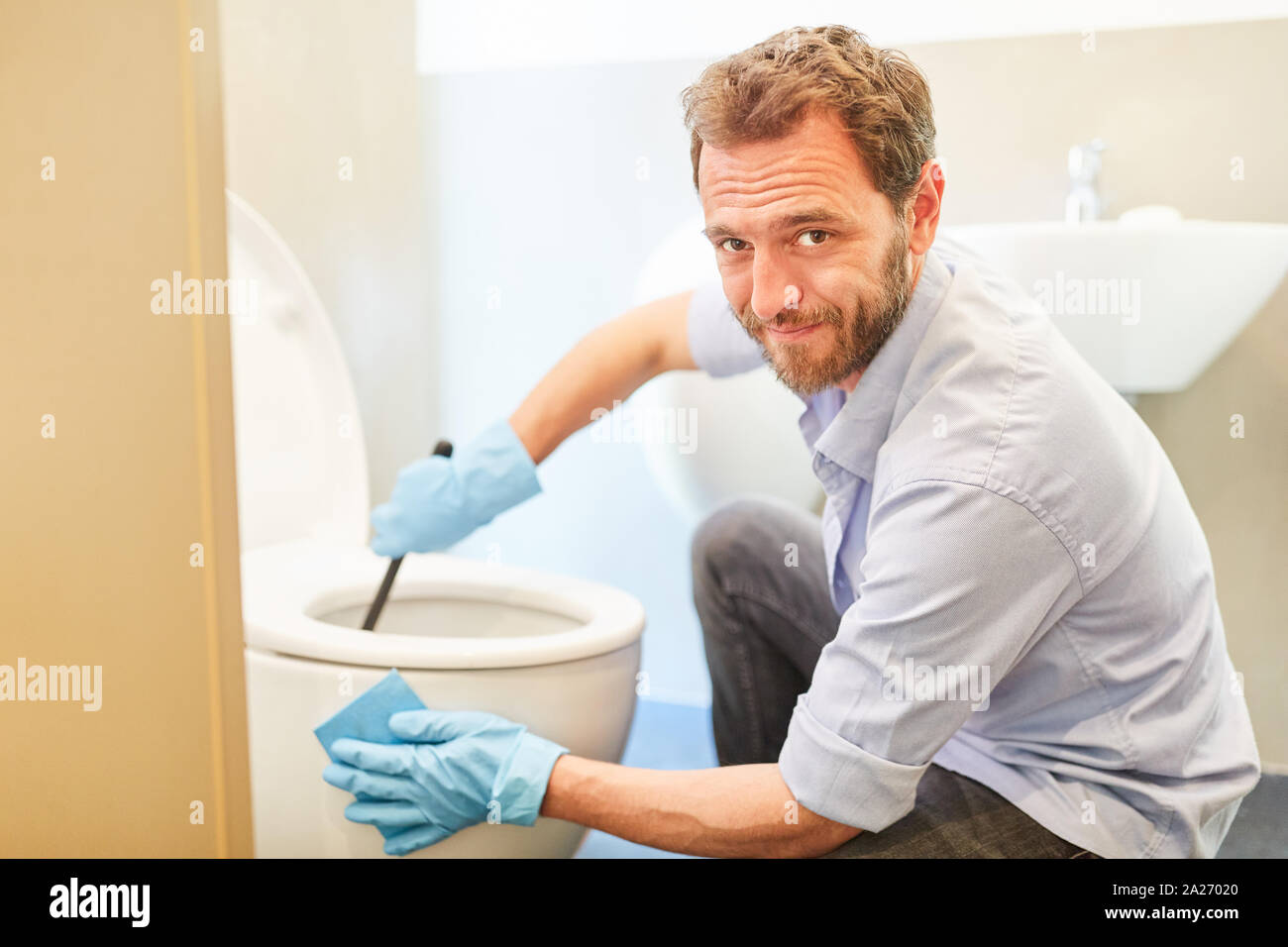 Man as a housekeeper cleans toilet or WC in the bathroom for new role distribution Stock Photo