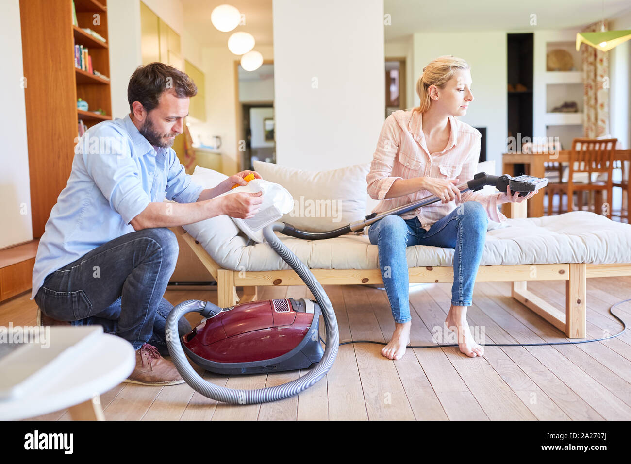 Young couple with vacuum cleaner in the living room is doing spring cleaning together Stock Photo