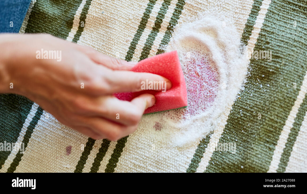 Hand with a sponge and salt while removing red wine stains on carpet Stock Photo