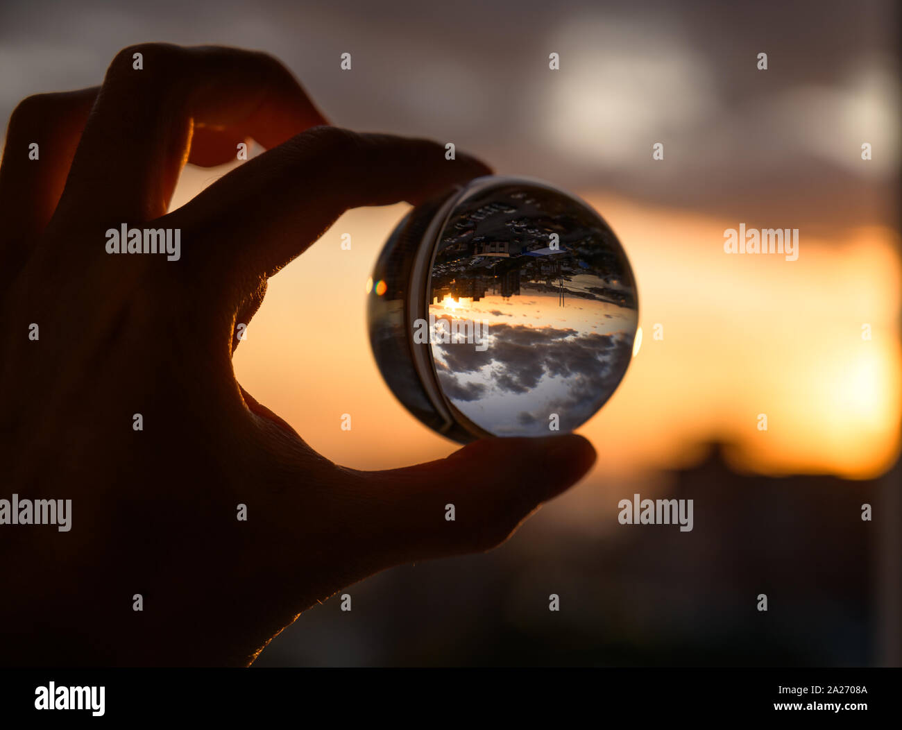 The hand holds glass ball which reflects sunset sky over city Stock ...
