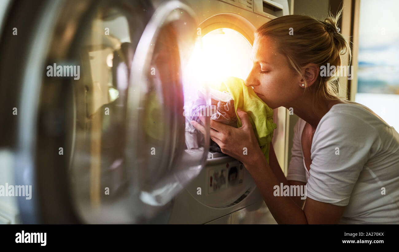 Woman at housework smells at fresh clothes from the clothes dryer Stock