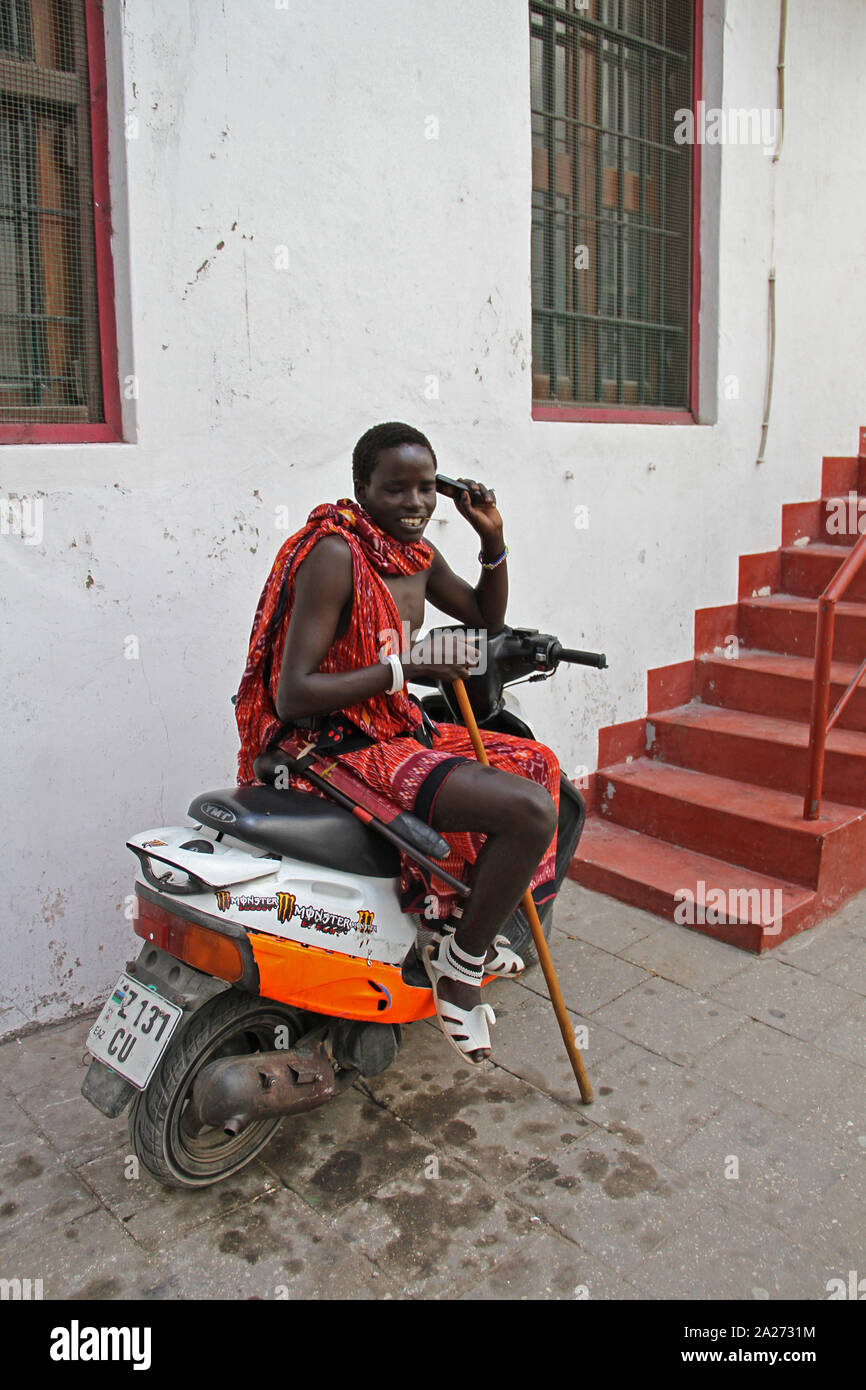 Traditional Masai man on scooter with a cellphone at the bottom of a staircase, Stone Town, Zanzibar, Unguja Island, Tanzania. Stock Photo