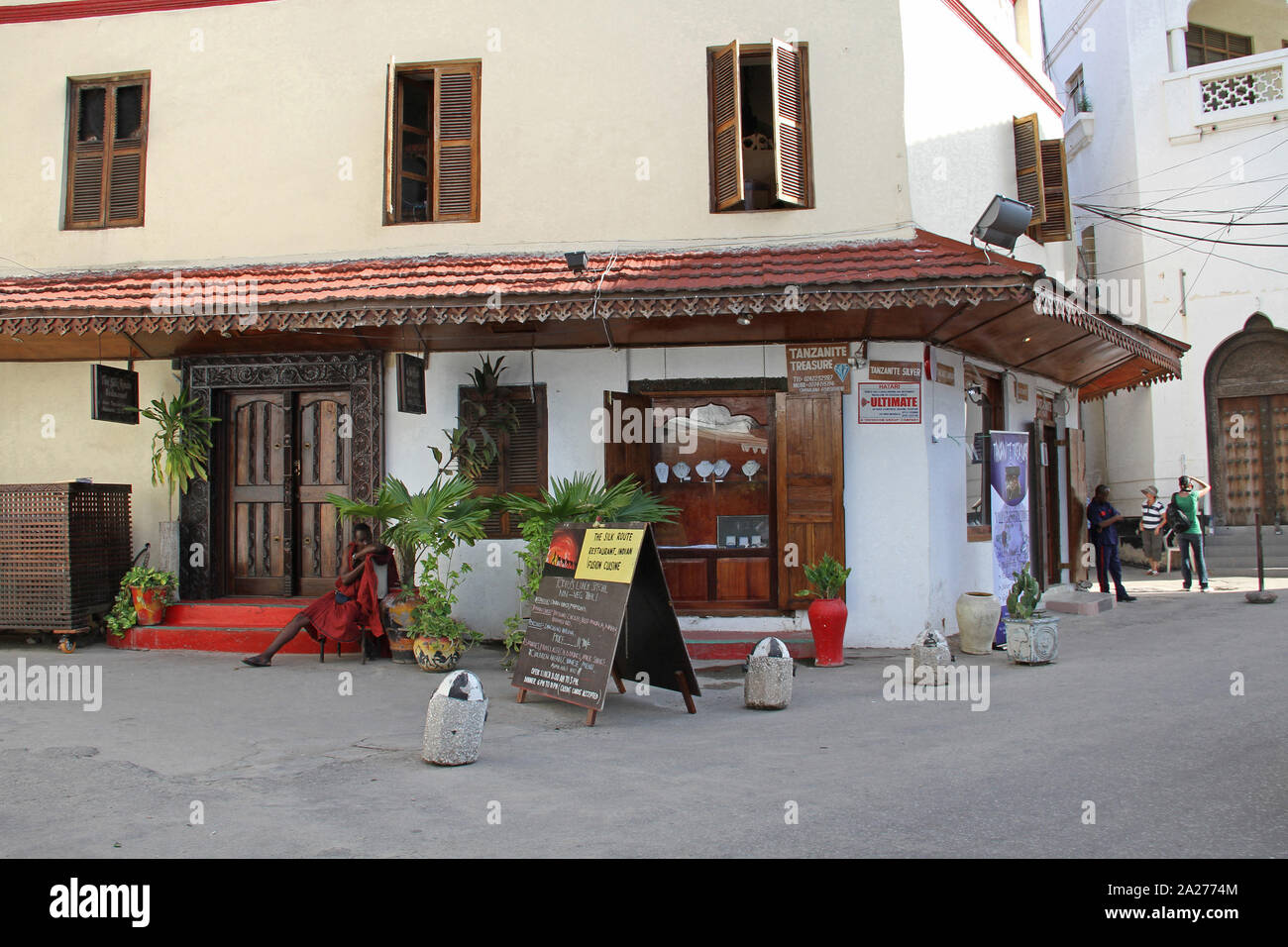 Maasai wearing red robe outside the Tanzanite Treasure jewellery store, Stone Town, Zanzibar, Unguja Island, Tanzania. Stock Photo