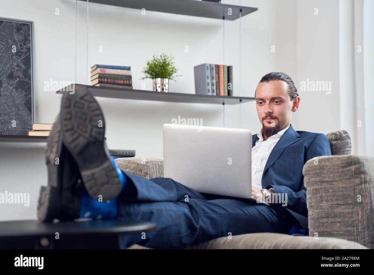 Image of serious businessman with laptop sitting on sofa in room during day Stock Photo