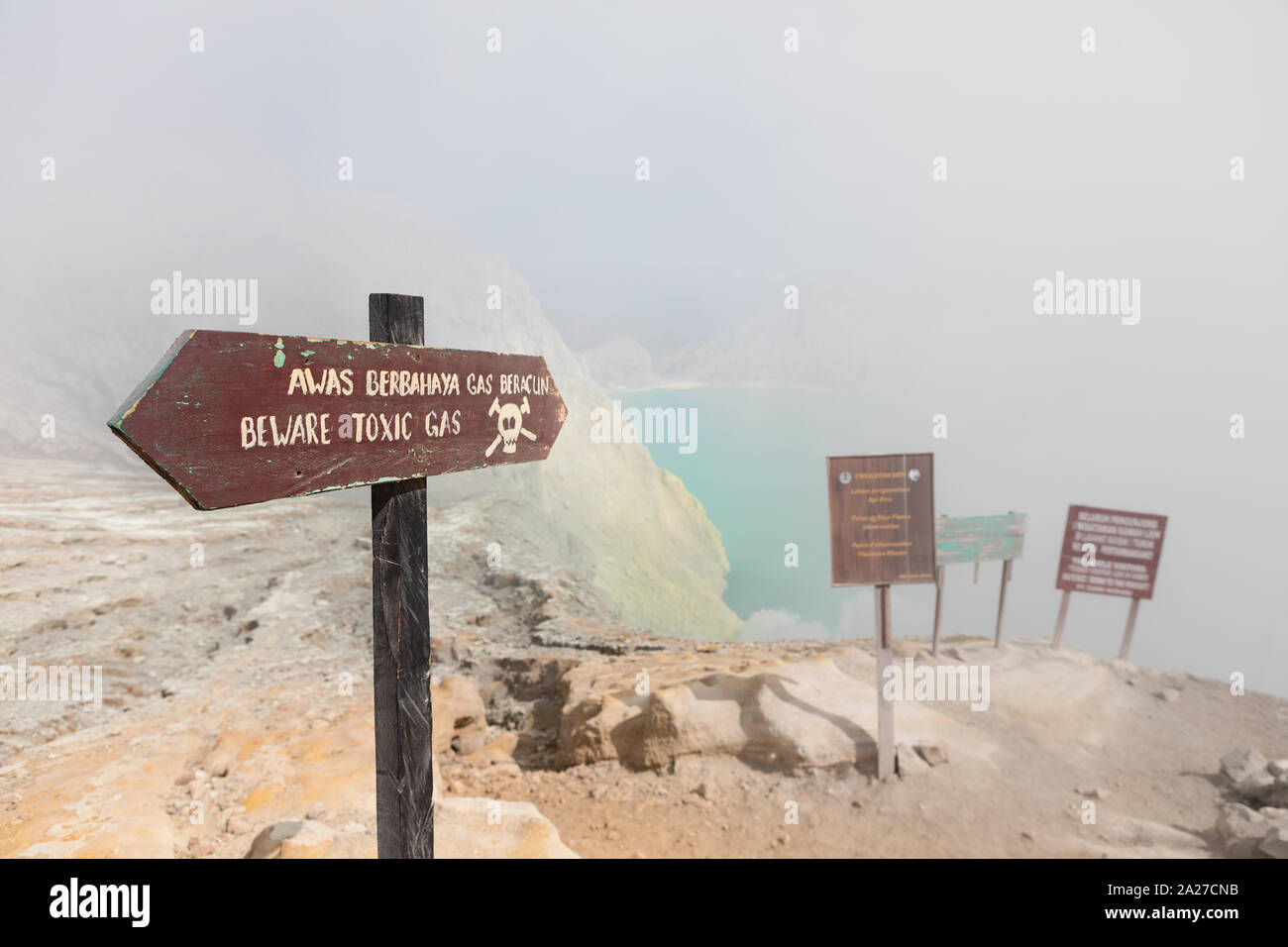 Warning signboard at wastelands in Kawah Ijen volcano crater at sulfur mine. Post apocalypse landscape with clouds of toxic gases from volcano Stock Photo