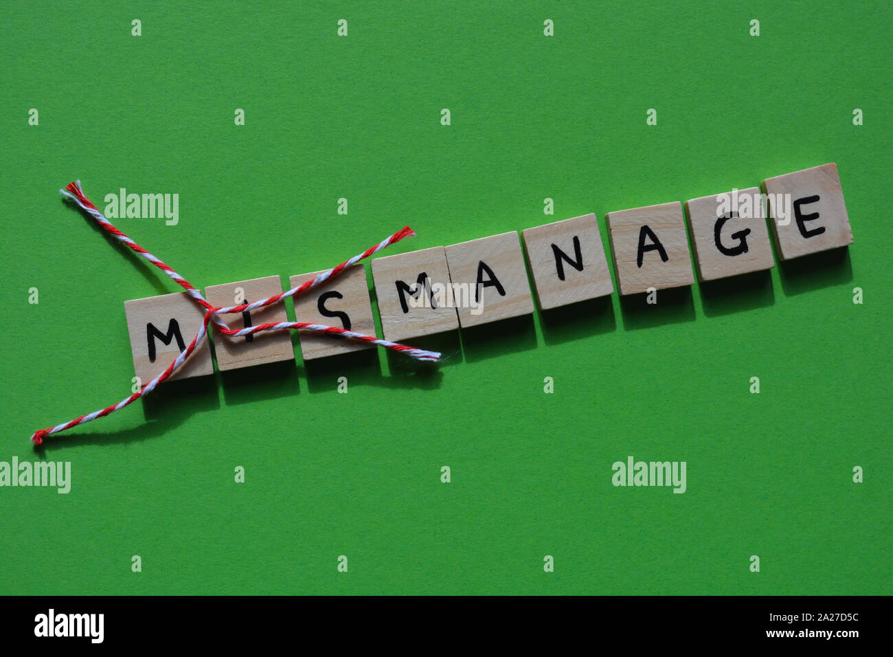 MisManage in 3d Wooden letters, with Mis crossed out, leaving the word Manage. Bright green background. Stock Photo