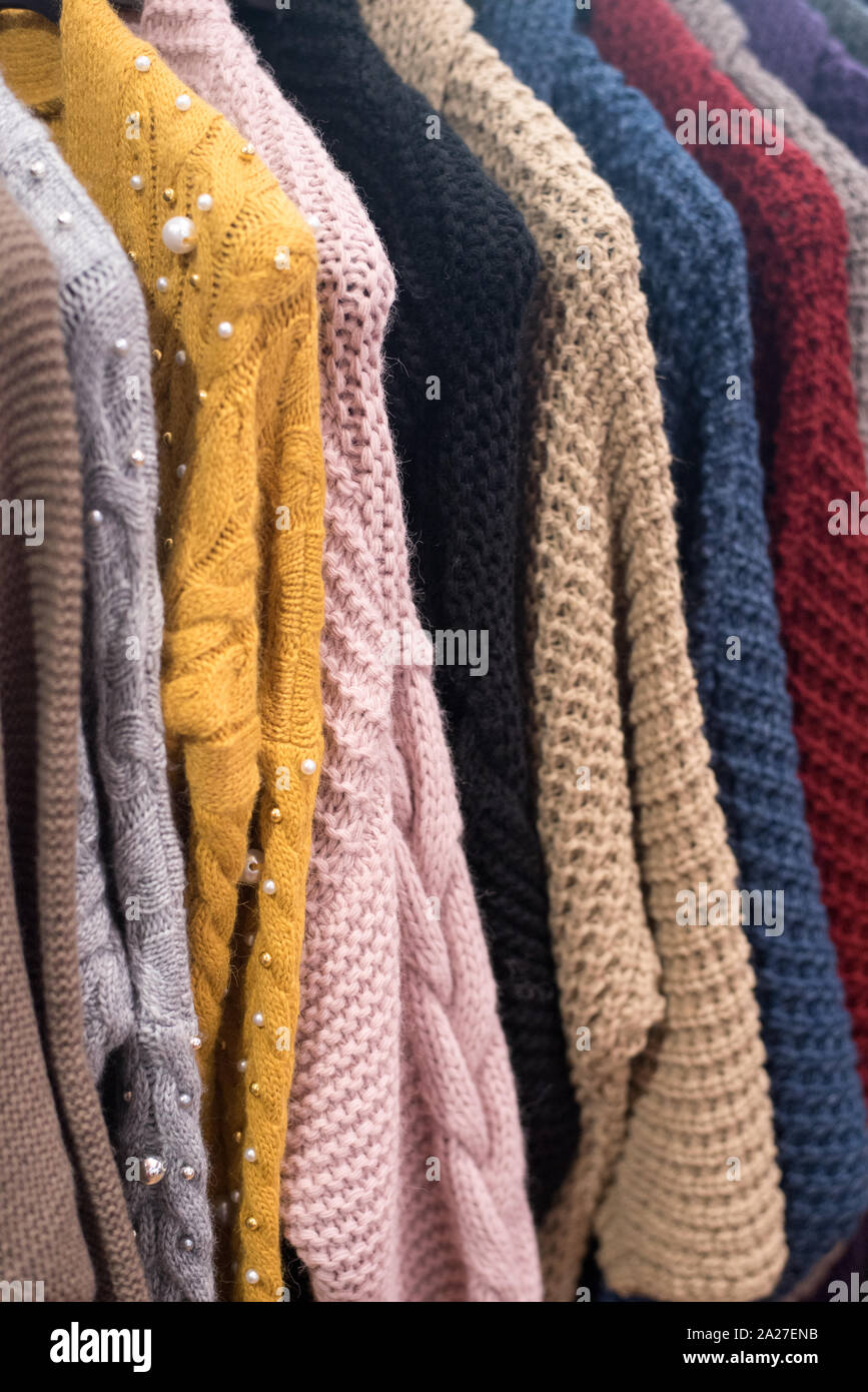 knitted sweaters and cardigans hang on a floor hanger. Colored big knitwear in the wardrobe Stock Photo