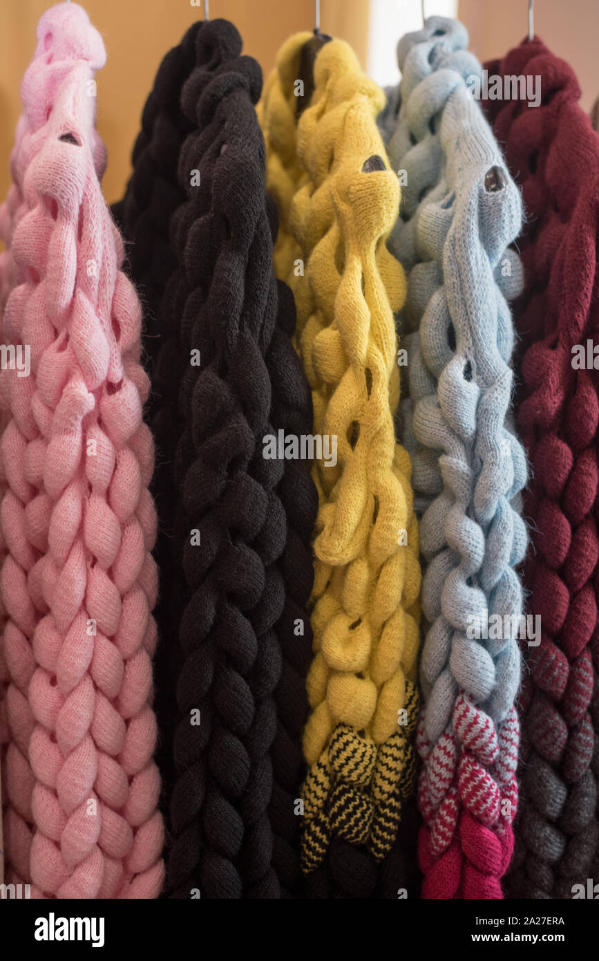 knitted sweaters and cardigans hang on a floor hanger. Colored big knitwear in the wardrobe Stock Photo