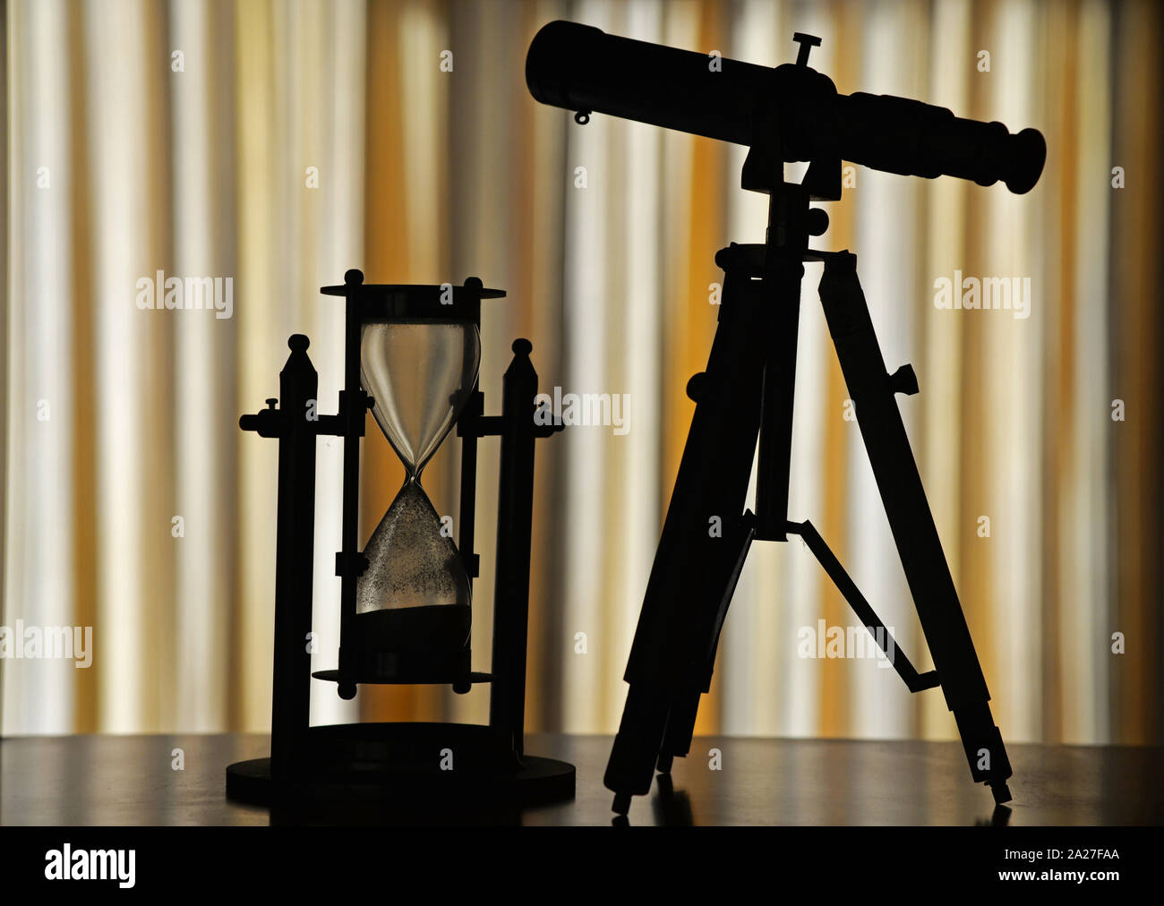 Silhouettes of a Hourglass and a telescope on a bookcase shelf. Concept : technology, exploration, science, observation, time etc. Stock Photo