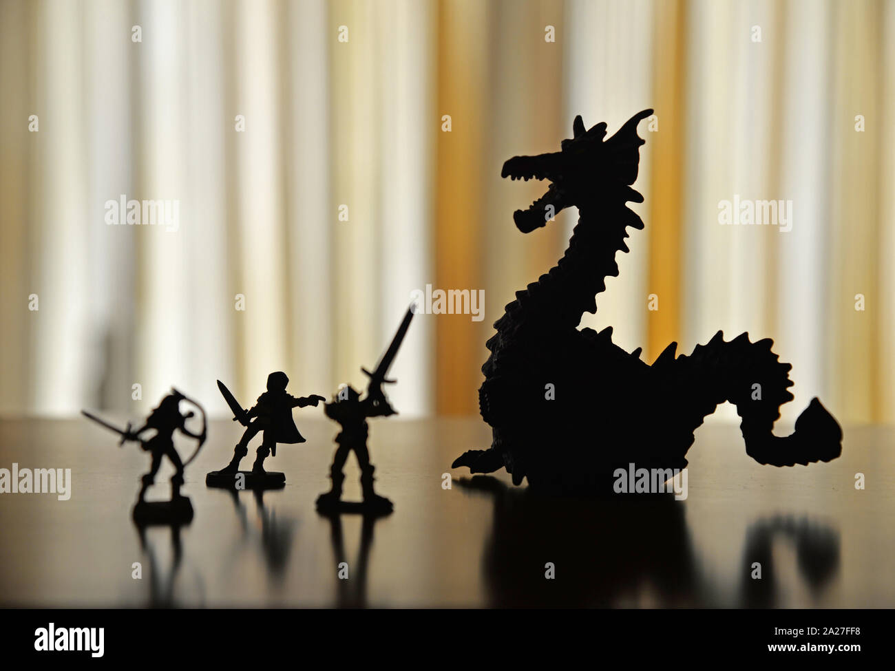 Silhouettes of a dragon and adventuring party figures on a bookcase shelf against a vivid yellow background. Stock Photo