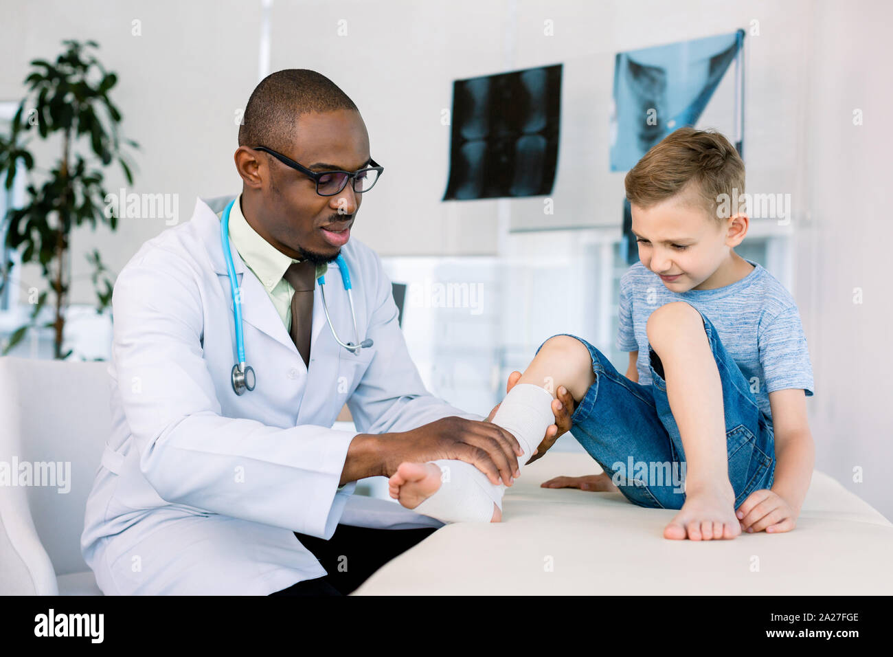 Coming to doctor. Little school boy coming to African man doctor after breaking his leg in the street. Leg in bandage Stock Photo